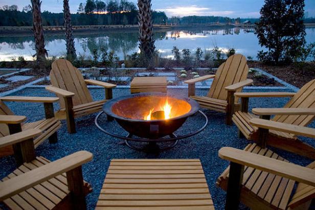 A metal fire pit surrounded by Adirondack chairs provides warmth alongside a beautiful view of a nearby lake.