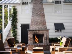 Comfortable outdoor lounge furniture surrounds this brick fireplace. The four wood chairs and two wood ottomans are each covered with chocolate brown fitted cushions.