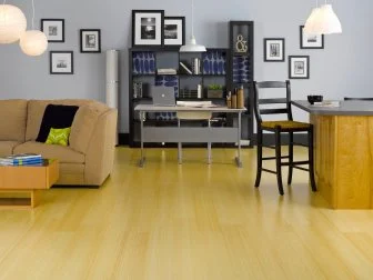 Wide view of office and living area with bamboo floor, gray wall, black shelving with desk and laptop, couch, asian lantern lights, and framed photos on wall. 