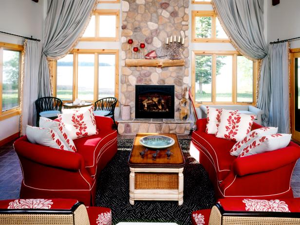 A pair of cherry red sofas brighten up this country living room. Floor-to-ceiling windows frame in the rustic stone fireplace and offer beautiful water views.