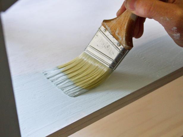 Man painting wooden shelf white.