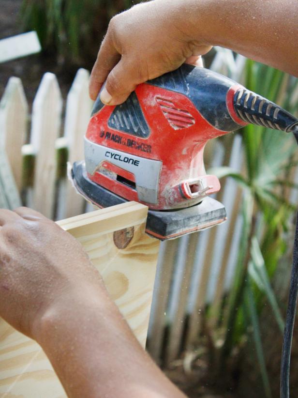 Man using a handheld power to sand lumber.