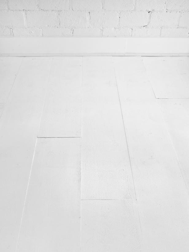 Wood floors painted white and white molding on a white brick wall .