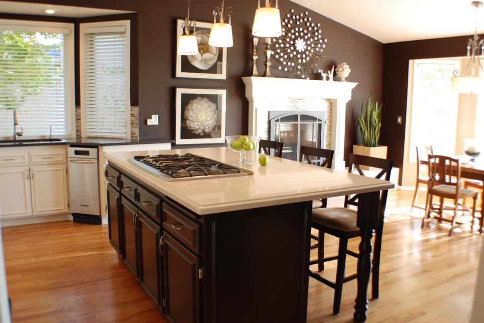 Open Plan Brown Kitchen With White Fireplace and Island With Cooktop