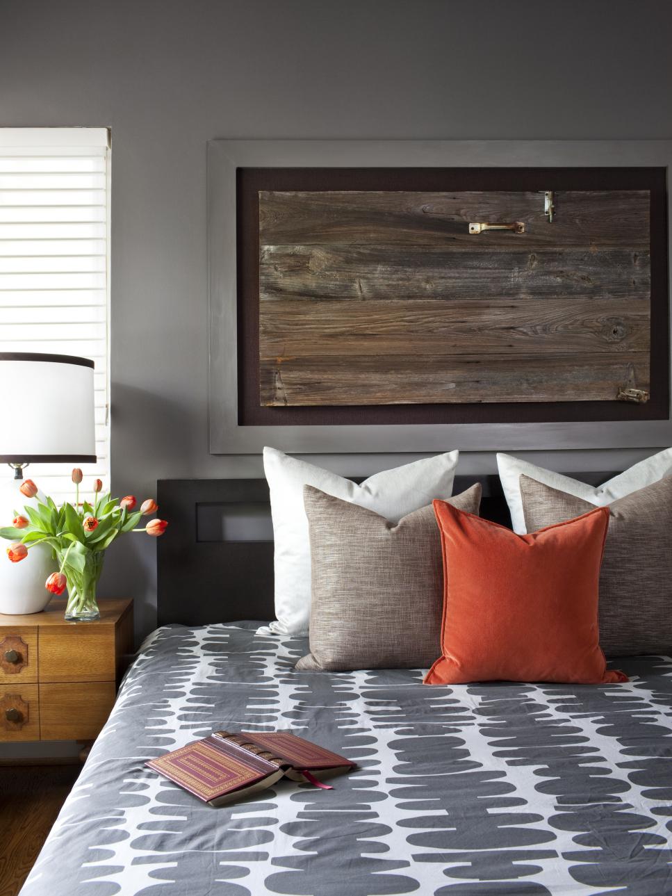Bedroom With Patterned Gray Bedding, Wood Wall Art and Orange Accents