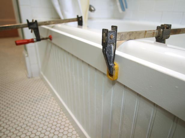 Press panel into place, then add clamps. Using caulk gun, add bead of silicone to gaps between panel and tub surround, wipe with damp cloth. Allow at least 24 hours for adhesive to dry.