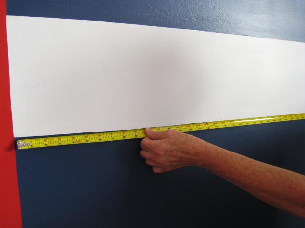 Decide on the monogram's letter size and font; print each letter onto standard printer paper. Measure wall area where letters will be painted; mark the center to help with placement. Tip: Give the monogram more graphic impact by placing the letters within a painted design; we chose to do a striped effect with painters' tape and red, white and navy latex wall paint.
