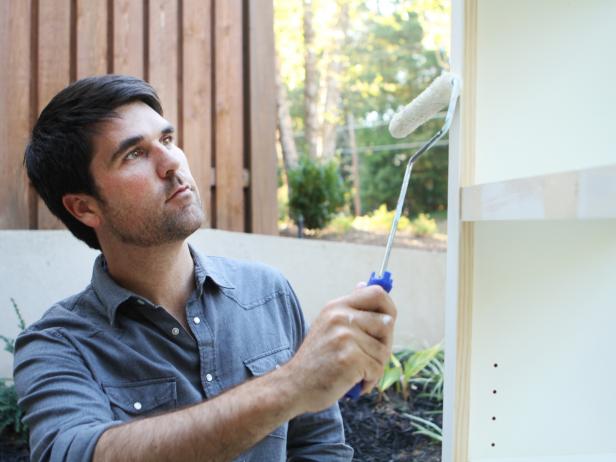 Once all trim is attached to front of bookshelves, fill any nail holes with spackle using putty knife and any gaps with caulk using caulk gun. Wipe away dust with damp cloth to assure clean surface. Sand lightly with medium-grit sanding block, then paint trim same color as bookshelf.