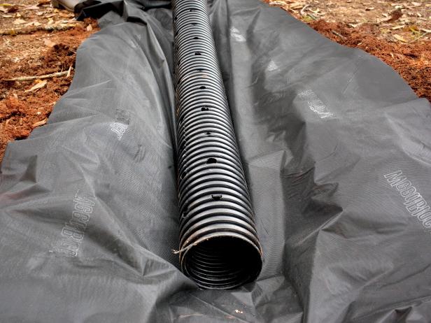 Lay the drainage pipe in a fabric lining in the dug ditch. Place drain pipe atop fabric lining, then add gravel, covering pipe completely. Leave approximately 5" between top of gravel and ground surface.