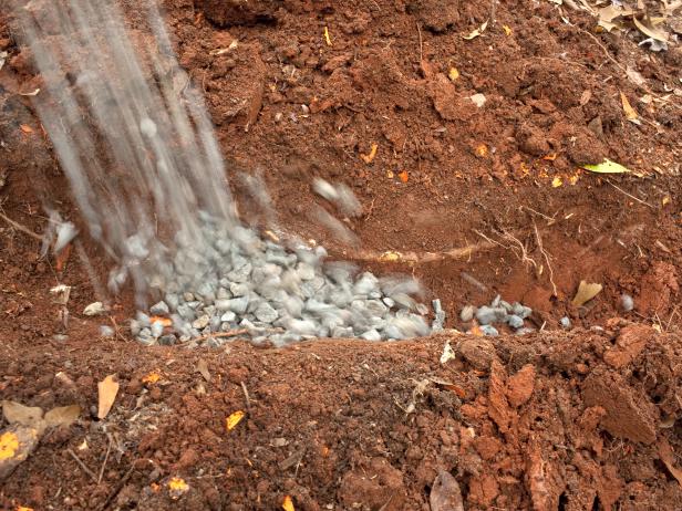 After digging a trench, place drainpipe atop fabric lining, add gravel layer and cover pipe completely. Leave approximately 5" between top of gravel and ground surface.