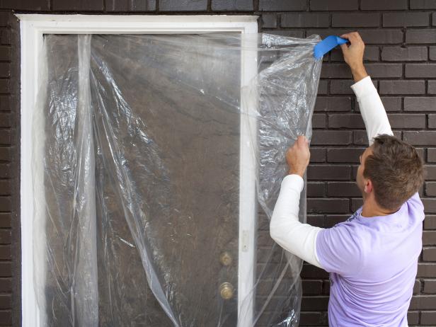 Man covering window with plastic before power washing a driveway.