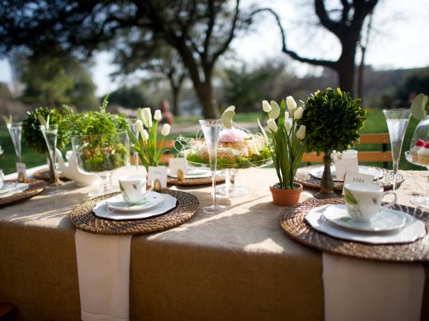 An outdoor tea party table setting, with white dishes and floral centerpieces.