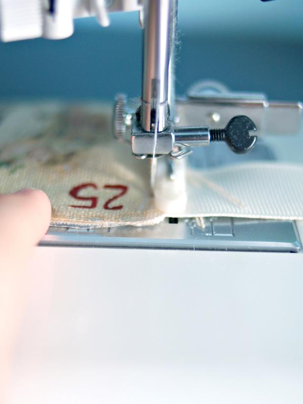 Sew along the graphic, ensuring ribbon is sewn into the pocket as well. Rotate the pocket and sew the bottom. Rotate again and sew up the left side. Insert ribbon at the upper left corner and finish sewing the pocket.