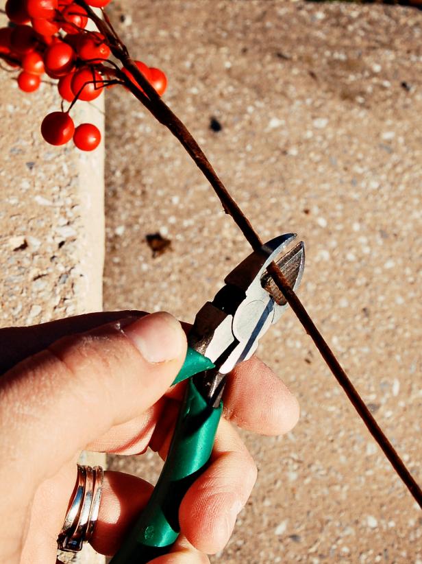 Clip and remove vine that wraps around smaller wreath. Gently spread vines apart with fingers and position small wreath on top of large pumpkin. Use wire cutters to trim five inches of wired stem off bottom of artificial bittersweet springs.