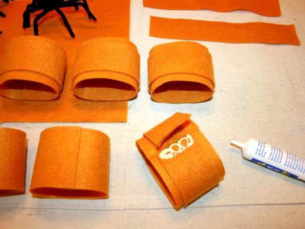 Glue is used to attach pipe cleaner spiders to Halloween napkin rings.