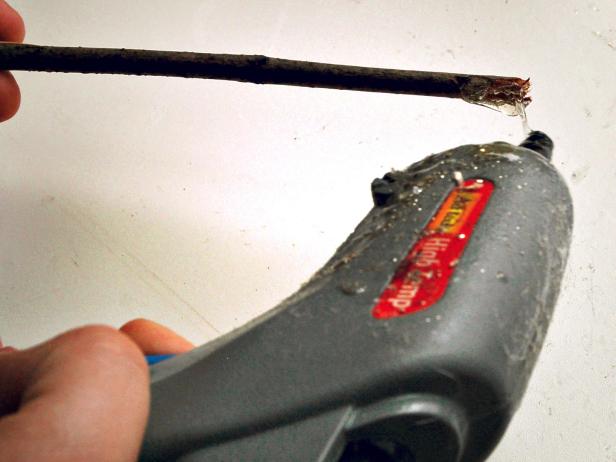 With a hot glue gun apply a bead of hot glue around bottom of stick in order to insert the stick into center of raffia bunch, ensuring raffia is evenly distributed around twig.