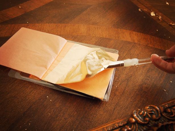 Use a soft brush to gently lift gold leaf sheet and apply to frame.