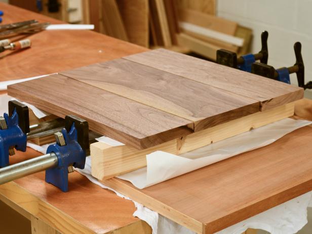 First, make sure wood isn't warped, is cut precisely and is smooth and square on all sides. Set two pieces of scrap wood (both the same size) on work surface. Place pieces of parchment paper over scrap wood to prevent cutting board pieces from sticking to scraps when glued. Place 16" x 6-3/4" piece in center with two 16" x 4-3/4" pieces on either side. Make sure to alternate the end grain to minimize warping; for example, the arc of the grain on the center piece should face up and the grain on the two end pieces should point down. Tip: Purchase wood boards from a mill or cabinet shop (rather than a hardware store) to ensure wood has been cut precisely.
