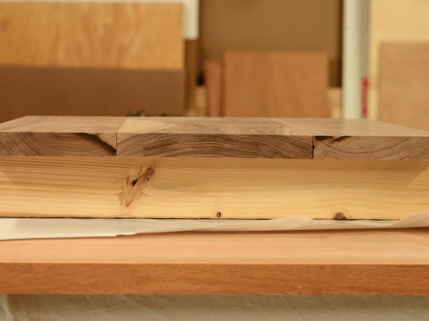 First, make sure wood isn't warped, is cut precisely and is smooth and square on all sides. Set two pieces of scrap wood (both the same size) on work surface. Place pieces of parchment paper over scrap wood to prevent cutting board pieces from sticking to scraps when glued. Place 16" x 6-3/4" piece in center with two 16" x 4-3/4" pieces on either side. Make sure to alternate the end grain to minimize warping; for example, the arc of the grain on the center piece should face up and the grain on the two end pieces should point down. Tip: Purchase wood boards from a mill or cabinet shop (rather than a hardware store) to ensure wood has been cut precisely.