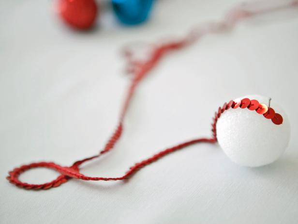 Start by creating the sequined balls that will hang on the bottom of the garland. Attach one end of the sequin trim pieces to a Styrofoam ball with a pin. Start wrapping the sequin trim around the Styrofoam ball.