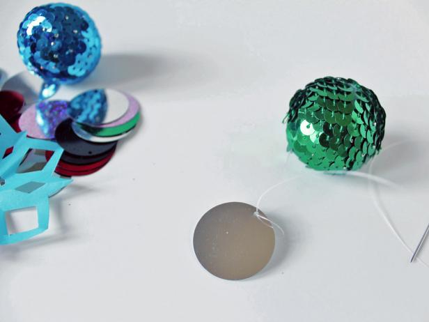 To create the garland, string a 30-inch piece of monofilament onto the sewing needle. Start with the sequin ball by threading the monofilament through a top section of it. Then, thread on some color sequins and snowflakes in a random pattern.