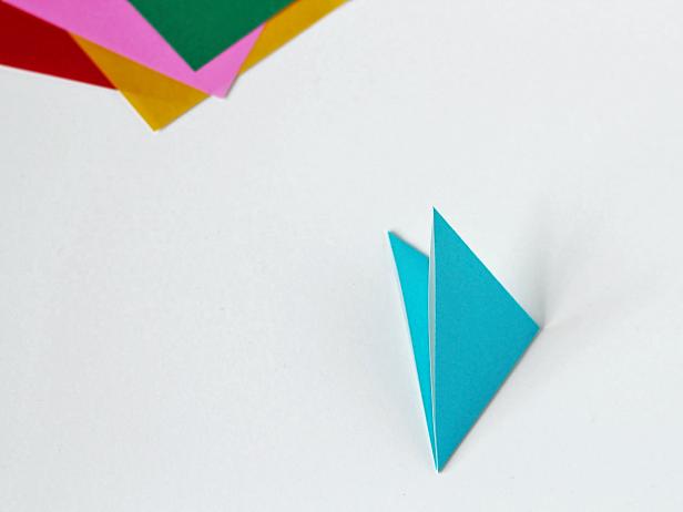 Fold a sheet of paper into a triangle. Then, fold that triangle into a smaller triangle. Fold each side point into the middle. Cut off the points. You now have a triangle-shaped piece that’s ready to fashion into a snowflake.