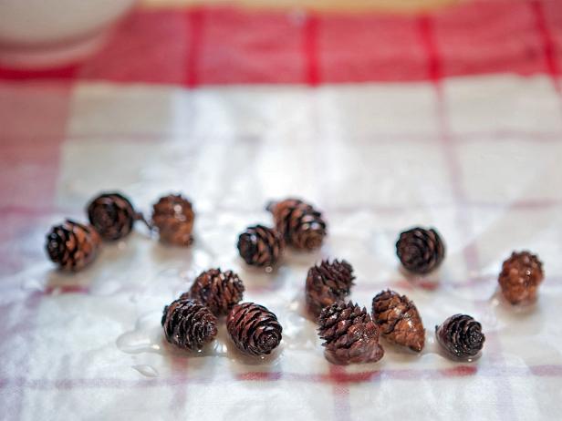 To make your own eucalyptus-pine firestarters, you will need paraffin or soy wax blend, eucalyptus essential oil, pine essential oil, green wax dye, miniature pinecones, flip-top glass jars, wax paper, kitchen towel, ivory cardstock, natural twine, double-boiler, and kitchen tongs. Melt the wax or paraffin over low heat in a double boiler. Add one teaspoon each of the eucalyptus and pine essential oils. Using tongs, dip each pinecone into the wax until it is fully covered. Let dry on the wax paper. Take the wax off the heat and add a few drops of the green dye. Keep adding dye until the wax reaches your desired color. Using tongs, dip individual pinecones into the green wax and let them dry on the wax paper. Fill a glass jar with the dried firestarters and tie on a hand-lettered label with twine.