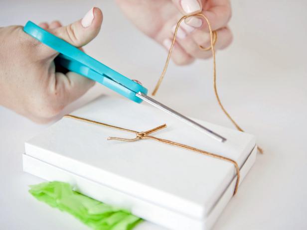Unfold the fringed tissue paper once and tie onto a gift box with a gold metallic cord. Knot the cord on the back and cut off any extra.