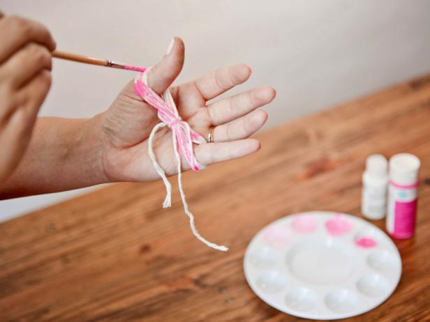 To create colorful twine for gift wrapping, start with a three yard piece of white cotton twine. In a figure eight pattern, criss-cross the twine around your thumb and pinky. Wrap the end around the center of the bundle. Pick any color and roughly paint it onto the twine in a random pattern. Remove the twine from your fingers and let dry. Unravel to tie around a gift box.