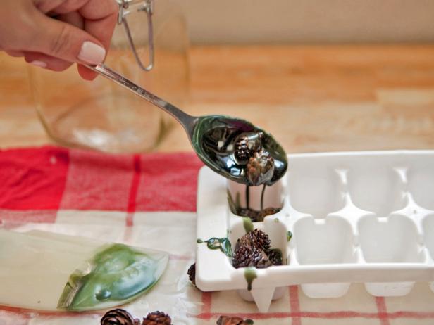 To make your own eucalyptus-pine firestarters, you will need paraffin or soy wax blend, eucalyptus essential oil, pine essential oil, green wax dye, miniature pinecones, flip-top glass jars, wax paper, kitchen towel, ivory cardstock, natural twine, double-boiler, and kitchen tongs. Melt the wax or paraffin over low heat in a double boiler. Add one teaspoon each of the eucalyptus and pine essential oils. Using tongs, dip each pinecone into the wax until it is fully covered. Let dry on the wax paper. Take the wax off the heat and add a few drops of the green dye. Keep adding dye until the wax reaches your desired color. Using tongs, dip individual pinecones into the green wax and let them dry on the wax paper. To create bunches of pinecones, pile several on a spoon and dip together. Drizzle with a little bit of extra wax and let dry in an ice cube tray. Fill a glass jar with the dried firestarters and tie on a hand-lettered label with twine.