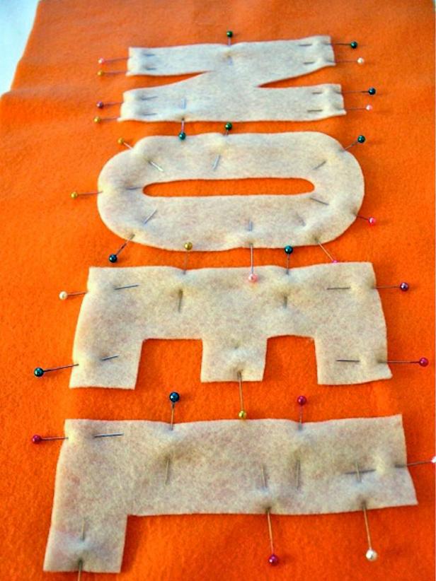 Cut out the felt letters and pin them in place on the pillow front. Using a sewing machine, sew each letter to the pillow front, leaving about 1/8 inch from the edge of the letter. When sewing circular letters don't tug the fabric or it will be stretched and wonky. Sew small bits at a time and then stop, lift your presser foot and allow the fabric to bounce back.