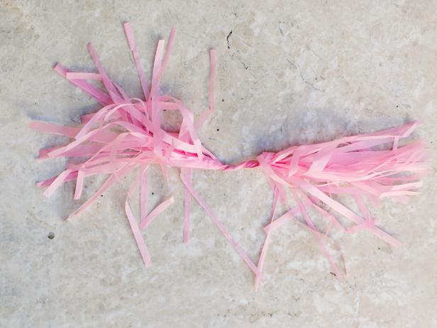 To make the tassels for your hanging garland, unfold tissue paper. Begin rolling tightly down the middle crease. Continue rolling, fold in half and then twist to create a loop for hanging.