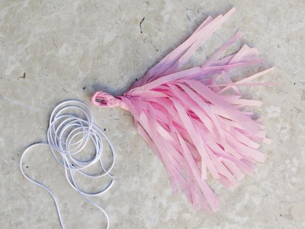 To twist the tassels for your garland, unfold tissue paper. Begin rolling tightly down the middle crease. Continue rolling, fold in half and then twist to create a loop for hanging.
