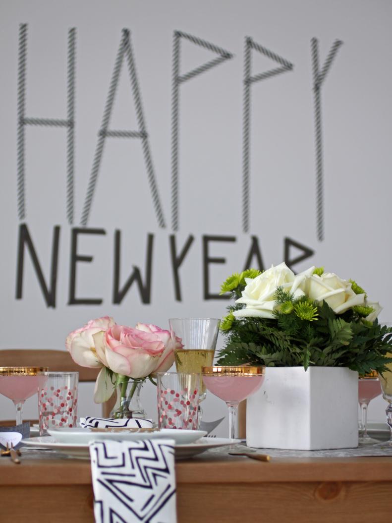 A table decorated with flowers, tableware, and a Happy New Year banner.