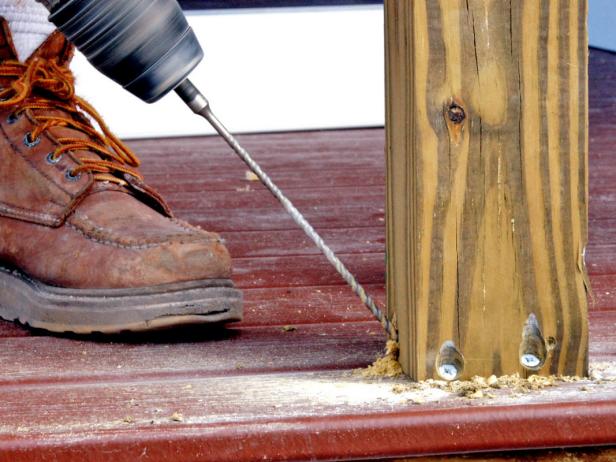 A wooden porch railing is screwed into place.