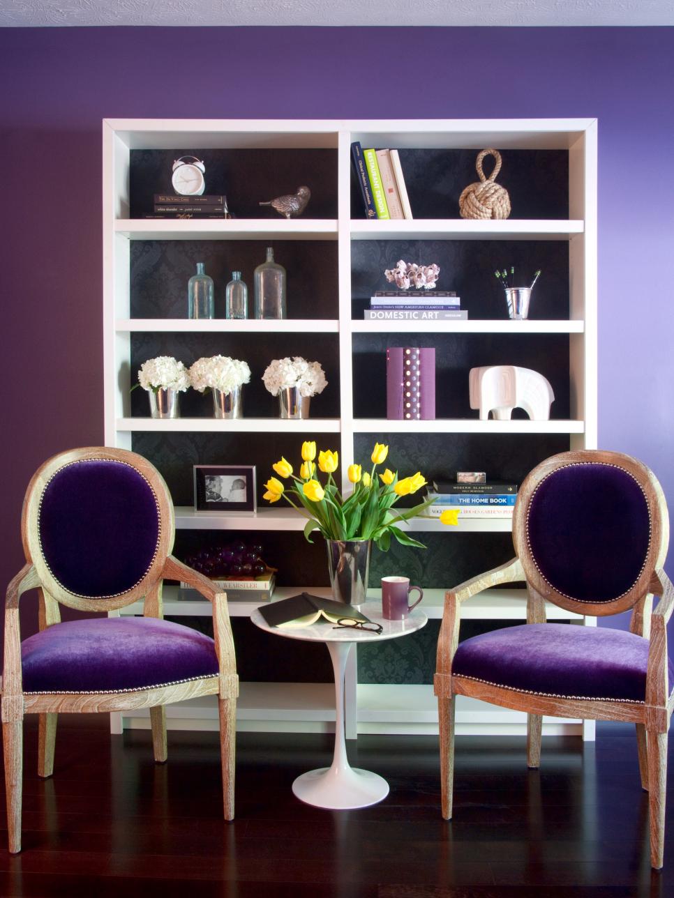 Eggplant Sitting Area With Yellow Flowers Purple room with white bookcase, velvet chairs and accessories.