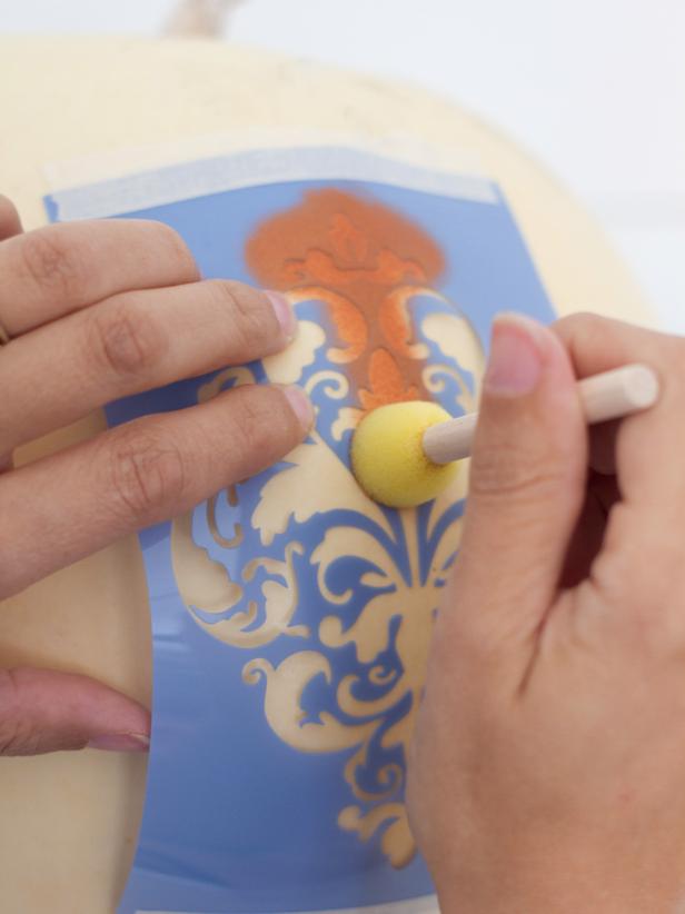 Load a stencil sponge brush with acrylic craft paint, then blot most of the paint off onto a paper plate. It's important to have a very "dry" brush when using stencils to prevent the paint bleeding under the stencil. Using a light hand, blot paint onto the center portion of the stencil. If any part of the stencil is raised up off the pumpkin, hold it down while continuing to blot. When finished, allow the painted portion to dry completely before moving on to the next step.