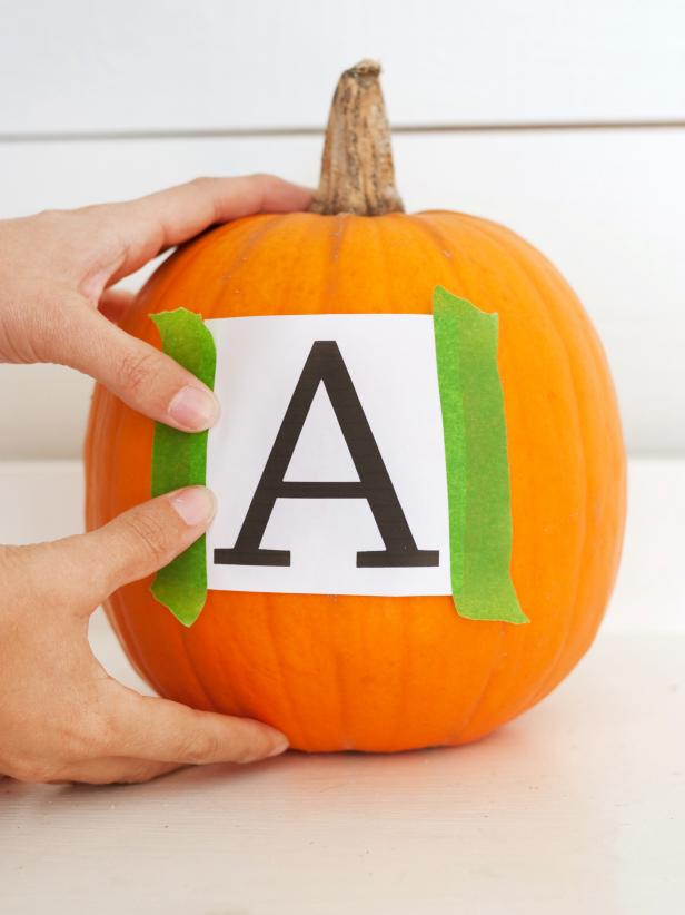 Measure the front side of your pumpkin to determine what size letter you'll need. Using your computer, select a font you like and print it out. Trim off most of the excess copy paper around the letter, then use painter's tape to attach the letter to the flattest side of the pumpkin.
