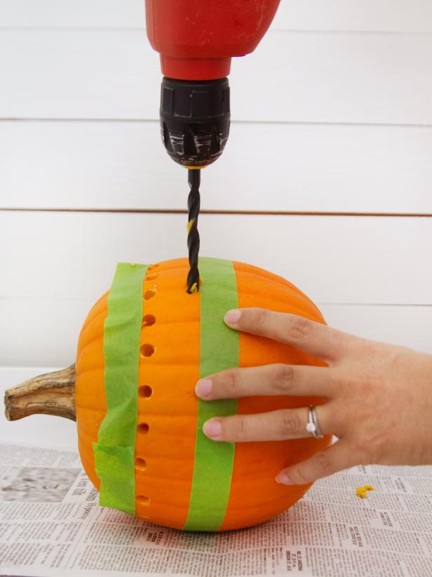 Use a large drill bit to drill holes into the pumpkin just under the top piece of painter's tape. Drill another row of large holes all the way around the pumpkin, just above the bottom piece of painter's tape. Remove both pieces of tape and drill a third row of large holes directly above the top row of holes.