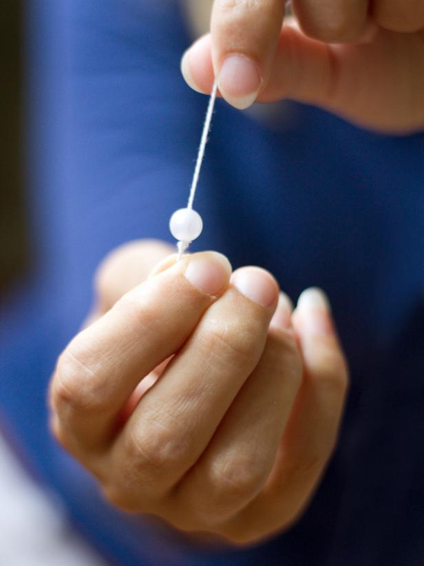 Thread twine through a craft pearl or decorative bead, then create a triple knot below the craft pearl or decorative bead to secure it.