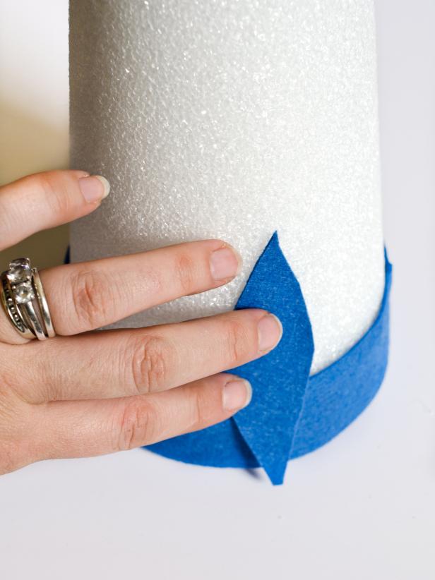 Apply hot glue in small sections around the base of each tree form and immediately press strip of darkest felt in place. Just above felt strip, apply a bead of hot glue vertically and immediately press the darkest felt feather into glue. Hold in place for few seconds until glue cools. Repeat with other dark felt feathers, placing them side by side so they slightly overlap, concealing the cone. Once the entire bottom row is finished, start a second row of dark felt feathers just above first row. Continue to glue feathers on, graduating from dark to light in rows of two. Tip: Use a moderate amount of hot glue. You don't want glue to squeeze out when felt feathers are pressed down.