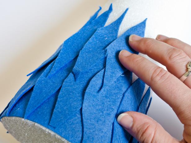 Apply hot glue in small sections around the base of each tree form and immediately press strip of darkest felt in place. Just above felt strip, apply a bead of hot glue vertically and immediately press the darkest felt feather into glue. Hold in place for few seconds until glue cools. Repeat with other dark felt feathers, placing them side by side so they slightly overlap, concealing the cone. Once the entire bottom row is finished, start a second row of dark felt feathers just above first row. Continue to glue feathers on, graduating from dark to light in rows of two. Tip: Use a moderate amount of hot glue. You don't want glue to squeeze out when felt feathers are pressed down.
