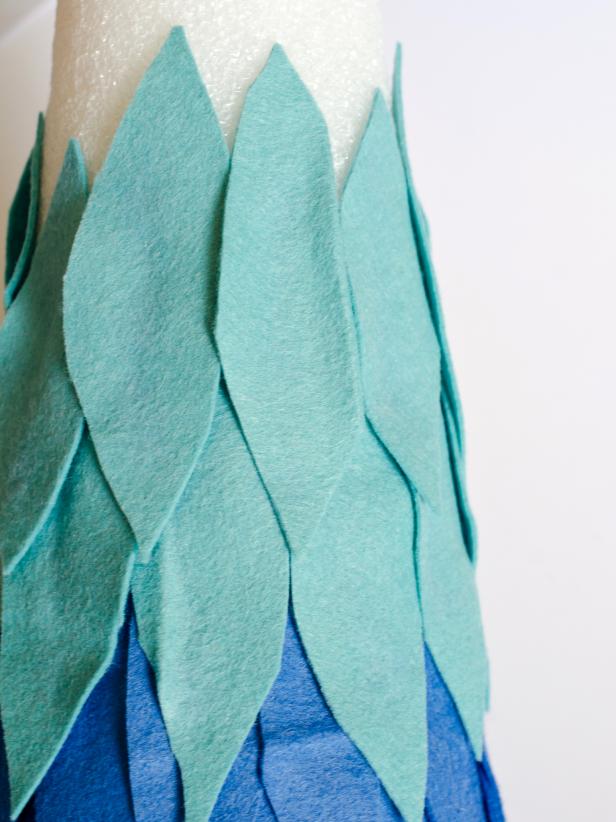 Apply hot glue in small sections around the base of each tree form and immediately press strip of darkest felt in place. Just above felt strip, apply a bead of hot glue vertically and immediately press the darkest felt feather into glue. Hold in place for few seconds until glue cools. Repeat with other dark felt feathers, placing them side by side so they slightly overlap, concealing the cone. Once the entire bottom row is finished, start a second row of dark felt feathers just above first row. Continue to glue feathers on, graduating from dark to light in rows of two. Tip: Use a moderate amount of hot glue. You don't want glue to squeeze out when felt feathers are pressed down.