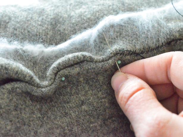 Gently insert pillow form in cover, making sure it fills cover to each corner. Fold raw edges of opening inside pillow cover and pinch together, pinning it shut. Stitch your Halloween cobweb pillow shut with a needle and thread. Use a whipstitch to sew edges closed with an all-purpose sewing needle and dark gray all-purpose cotton thread. Remove pins and trim any loose threads.