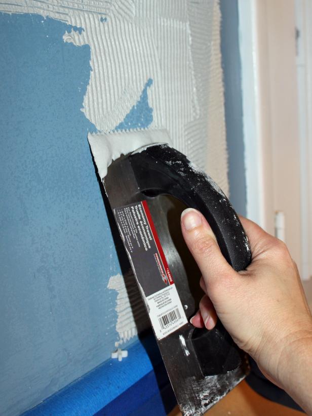 First, lay a spirit level on the existing countertop area to ensure it is level. If not, note where it dips or rises so you can accommodate with a wider caulk line where needed between the tile and countertop. Dip notched trowel into mortar, then spread an even layer onto a small section of wall.