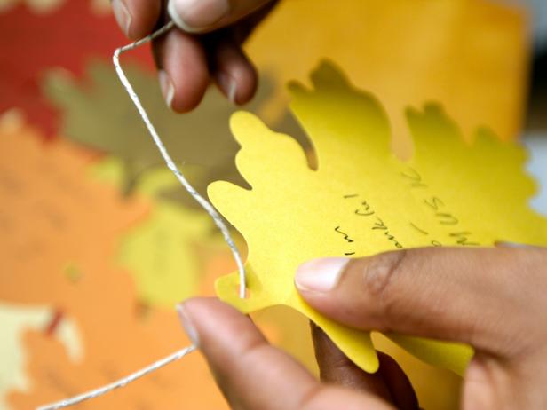 Thread the cut twine through the hole in each leaf. Bring both ends of the twine together to create a loop and knot at the top of the loop. Tip: Purchase twine in a variety of colors, from gold to silver to black and white. The twine can add to the colorful mix on your thankful tree.
