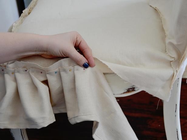 Return slipcover to chair, still positioned inside out. Start at center chair front and pin center point of the skirt top to the slipcover seat. Make sure raw edges are pointing in the same direction. Pinch skirt fabric with fingers to pleat and pin in place, following the lines of the chair seat. Continue around the skirt, pleating and pinning.