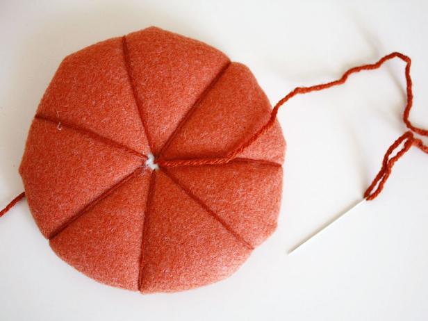 Poke a hole in the center of the cardboard, then thread a needle with orange yard to create seams on your pumpkin.
