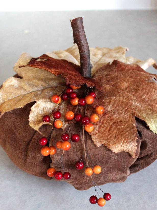 Now finish off by adding accessories. You can use a twig from your backyard and cut it down to the desired size. Hot glue the accessories into place over the hole on the top of the pumpkin. Next, add velvet leaves from the craft supply store.