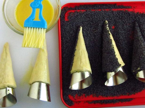 Place poppy seeds in a shallow dish. Brush cones of dough with egg wash, then roll them in poppy seeds, being sure to completely cover the cone. If you have bare spots, carefully add more egg wash, then press the poppy seeds onto the dough with your fingers.